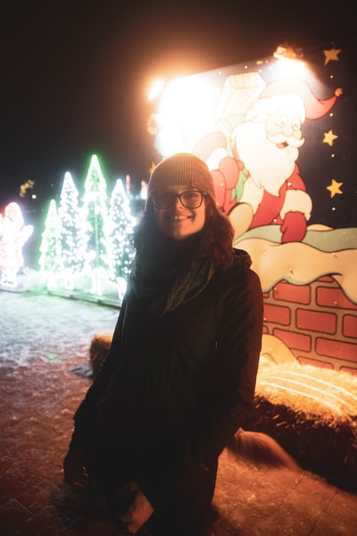 穿着黑色夹克的女人站在点亮的圣诞树旁